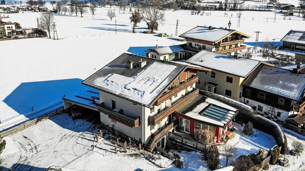 A snow-covered village with traditional buildings, including a multi-story house with balconies and a red building with a large window. - Rupertus by Interhome (Zell am See)