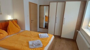 A hotel room with two beds, orange bedding, a wooden floor, and a large wardrobe. - Rupertus by Interhome (Zell am See)
