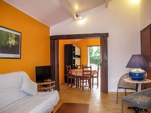 Una habitación con sofá, televisión, mesa de comedor con sillas, lámpara y un cuadro en la pared.