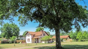 Een huis met een grote boom ervoor, omringd door een grasveld en andere gebouwen.