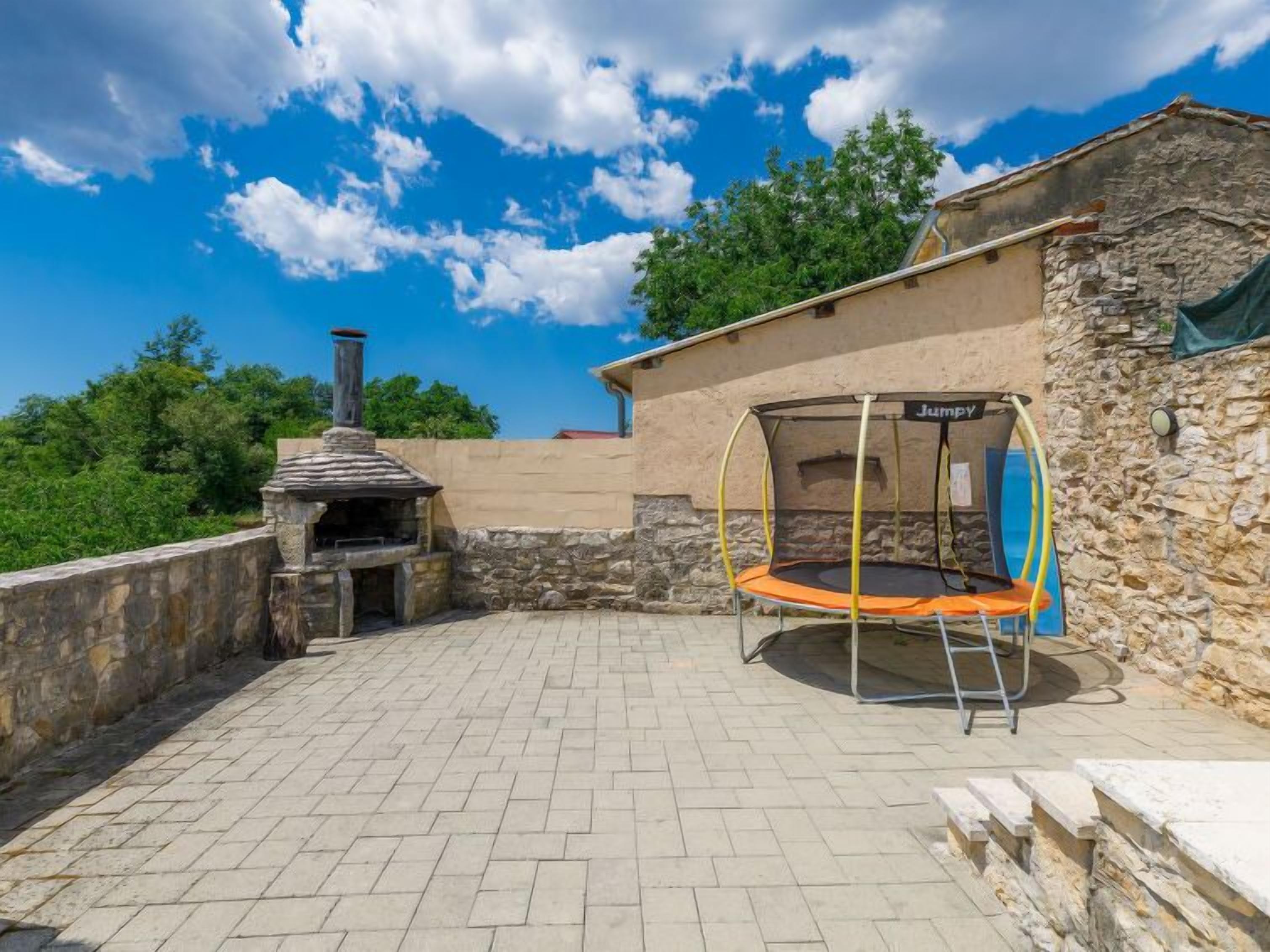 An outdoor patio with a stone oven, a trampoline, and a stone wall.
