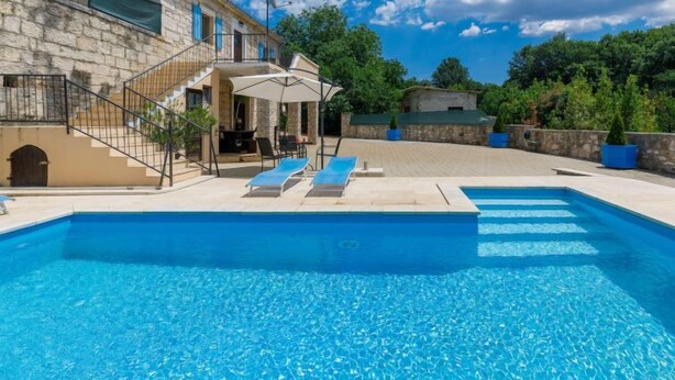 Um edifício de pedra com piscina, área de estar ao ar livre e escadaria que leva a uma varanda.