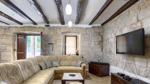 Uma sala de estar aconchegante com um amplo sofá seccional bege, uma pequena mesa de centro de madeira e uma televisão de tela plana fixada na parede de pedra.