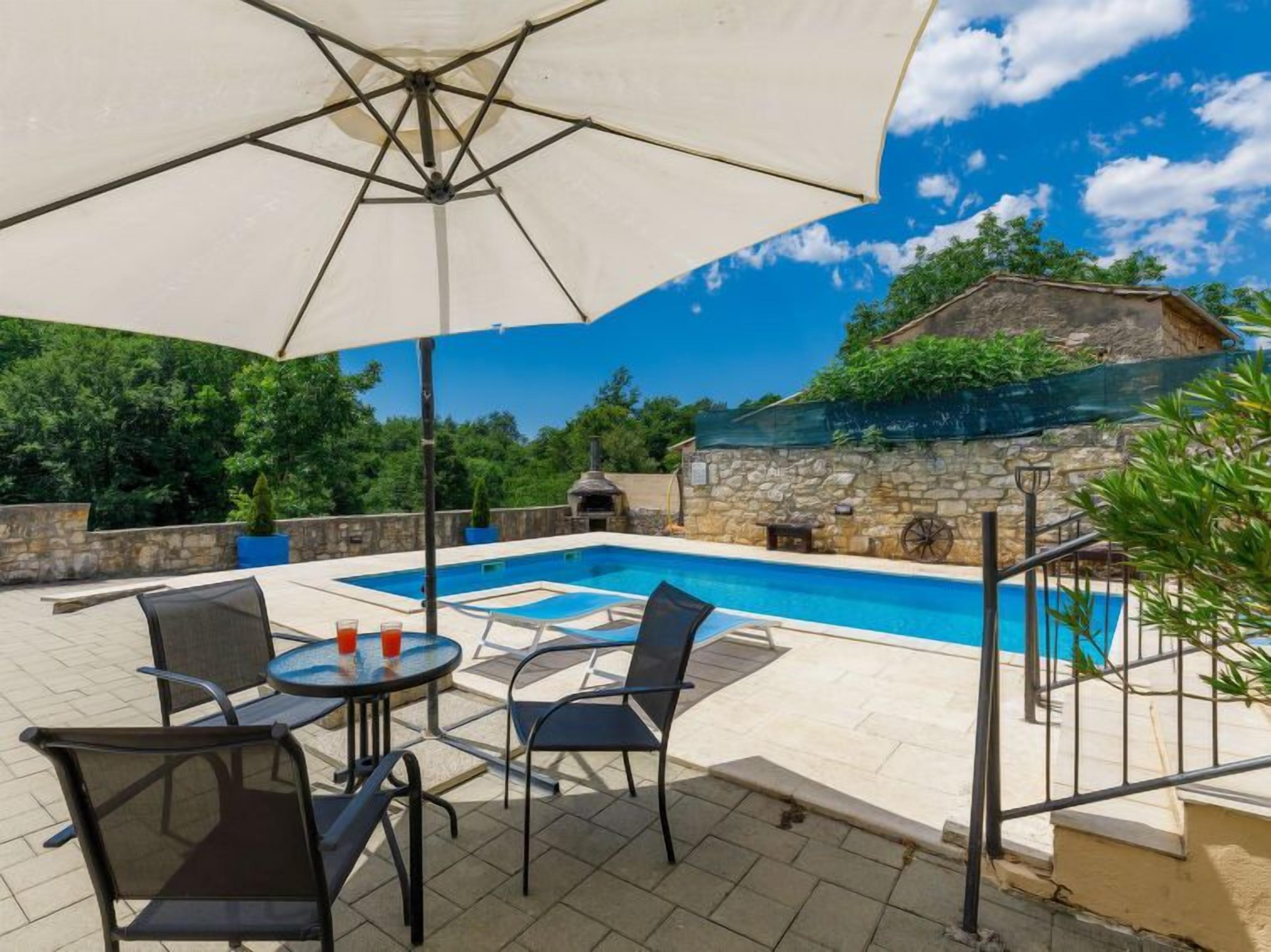 A pool area with a table and chairs, a large umbrella, and a stone wall in the background.