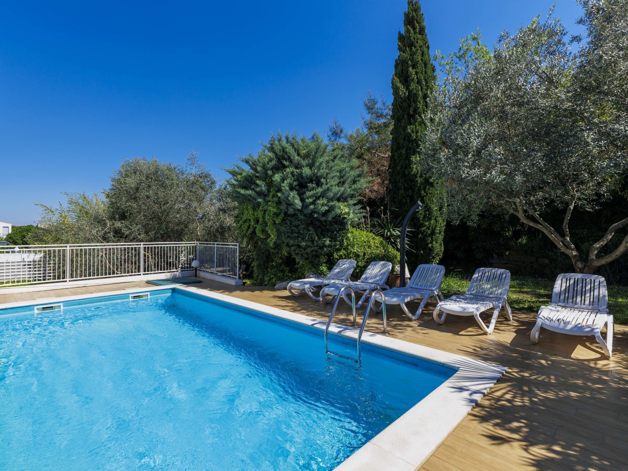 A swimming pool with lounge chairs and a white fence.