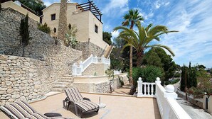 Een terras met lounge fauteuils, een stenen muur en een trap naar een gebouw.