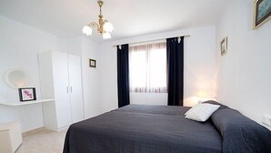 Een slaapkamer met een groot bed, een kledingkast, een nachtkastje, een lamp en een raam met gordijnen.