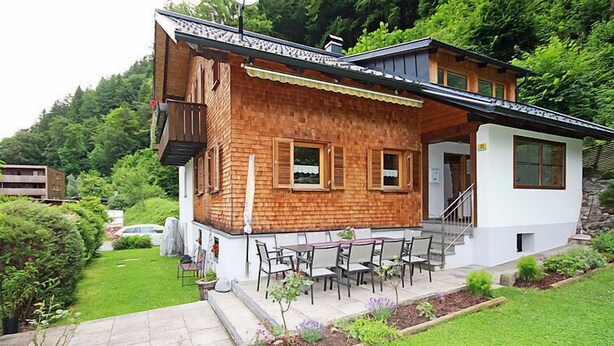 Ein zweistöckiges Holzhaus mit einer Terrasse, einer Treppe und einem Garten.