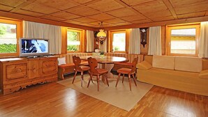 Ein Zimmer mit Holzwänden, einem Esstisch, Stühlen, einer Couch und einem Fernseher.