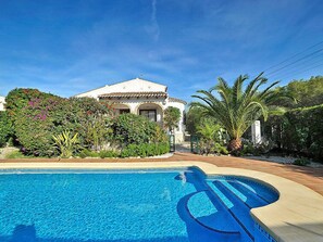 A pool area with a clear blue pool, a white building with arches, and lush greenery including palm trees.