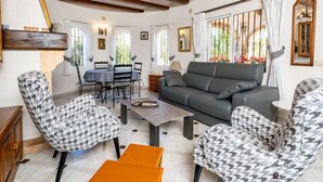 Un salon comprenant un canapé, deux fauteuils à motifs, une table basse et un coin repas avec une table et des chaises.
