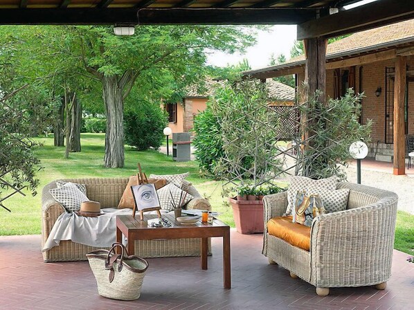 A covered outdoor seating area with wicker furniture, a table, and potted plants.