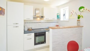 Une cuisine moderne avec des meubles blancs, un four encastré et un petit îlot central doté d’un plan de travail.