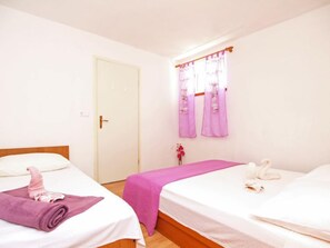 Ein Hotelzimmer mit zwei Betten, einer Tür und einem Fenster mit violetten Vorhängen.