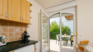 Eine Küche mit Kaffeemaschine, ein Essbereich mit Tisch und Stühlen sowie eine Glastür, die auf eine Terrasse im Freien führt.
