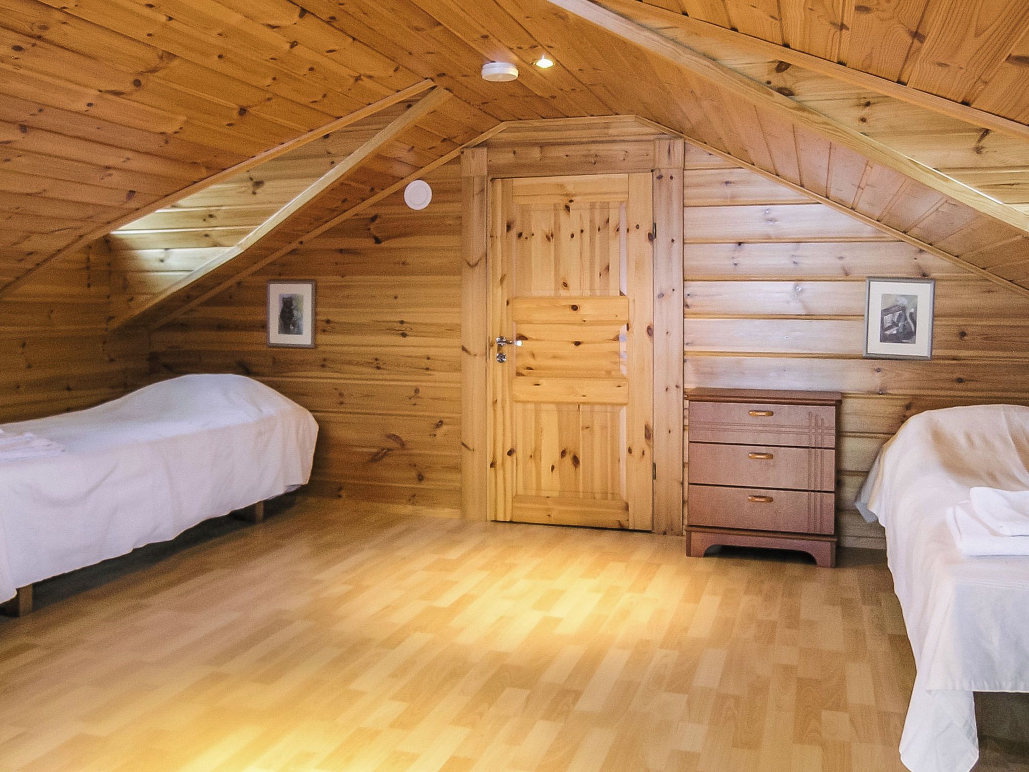 Una habitación de madera con dos camas, un aparador y una puerta.