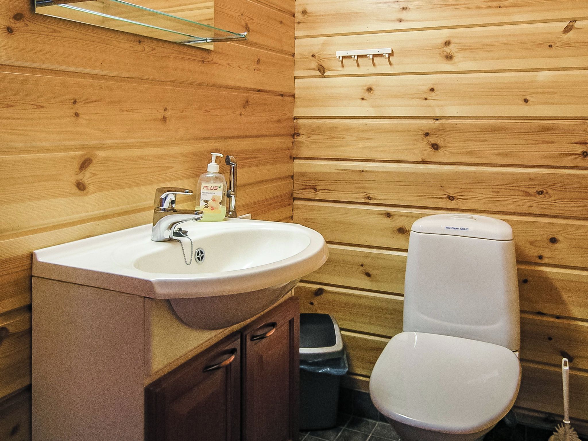 A wooden cabin-style bathroom with a sink, toilet, and a trash bin.