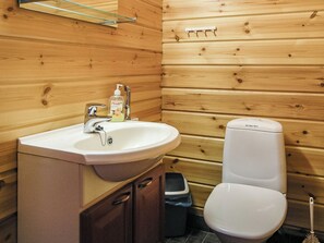 Une salle de bain de style rustique, avec des murs en bois, comprenant un lavabo, des toilettes et une poubelle.