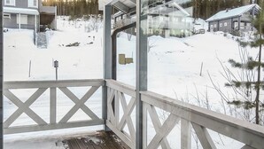 Une terrasse en bois dotée d’une rambarde, offrant une vue sur un paysage enneigé parsemé de maisons et d’arbres.
