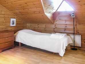 Une petite pièce agréable, avec un plafond en pente, un lit simple recouvert d’un drap blanc, une commode en bois et un radiateur.