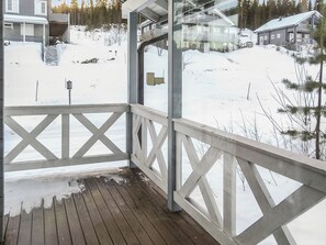 Una terraza de madera con barandilla, con vistas a un paisaje nevado con casas y árboles.