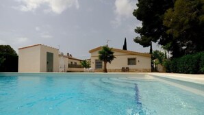 Una piscina con superficie de agua cristalina azul, rodeada por un edificio con techo de tejas y una palmera.