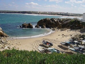 A beach with boats, rocky outcrops, and a distant shoreline.