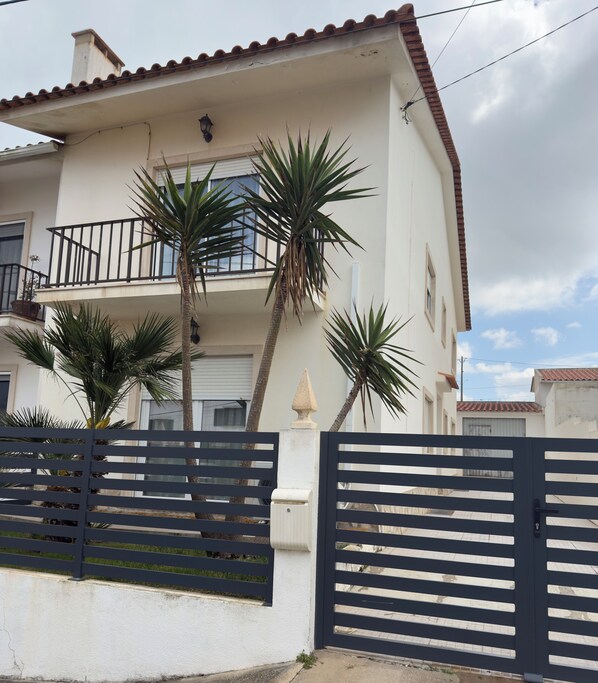A two-story building with a balcony, a gate, and palm trees.