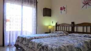 Une chambre avec deux lits, une fenêtre avec des rideaux légers et une lampe fixée au mur.