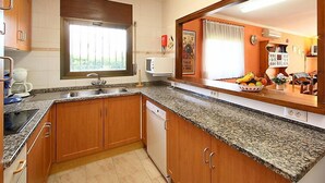 Une cuisine compacte avec des meubles en bois, un plan de travail en granit, un lave-vaisselle encastré et une fenêtre équipée de stores.