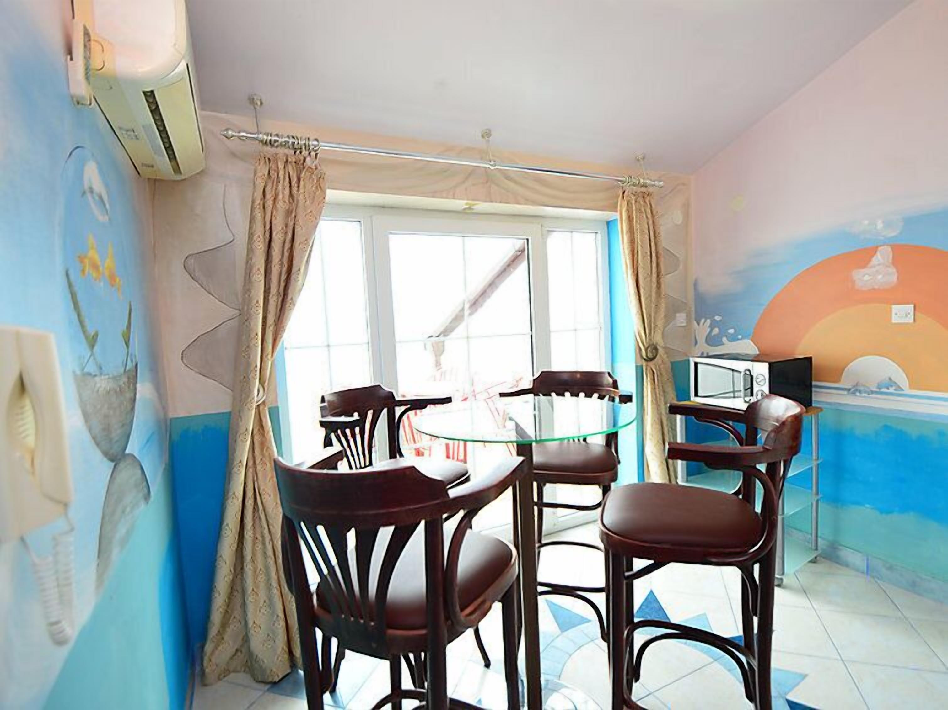 A dining area with a round glass table and four wooden chairs, a microwave on a counter, and a window with curtains.