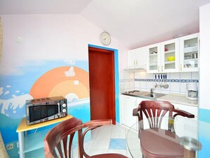 Une petite cuisine équipée d’un four à micro-ondes, d’un évier et de placards. On y trouve une table à manger avec des chaises, et un mur décoré d’une fresque.