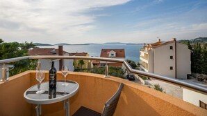 Un balcone con tavolo, bicchiere da vino e bottiglia, vista su un corpo d'acqua e edifici.