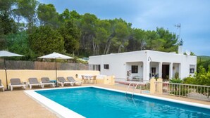 Una piscina rectangular con zona de borde en blanco, sillas de descanso y sombrillas.