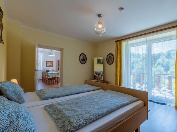 A bedroom with two beds, a dining area, and a balcony with a view.