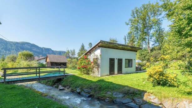 A small house with a stone bridge over a stream, surrounded by greenery and mountains. - Apartment Pacher by Interhome (Gallizien)