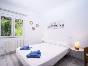A bedroom with a large bed, two bedside tables with lamps, a radiator, and a window with a view of greenery.
