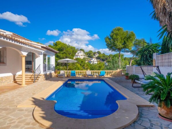 A swimming pool with a stone deck, lounge chairs, and a view of houses in the background.