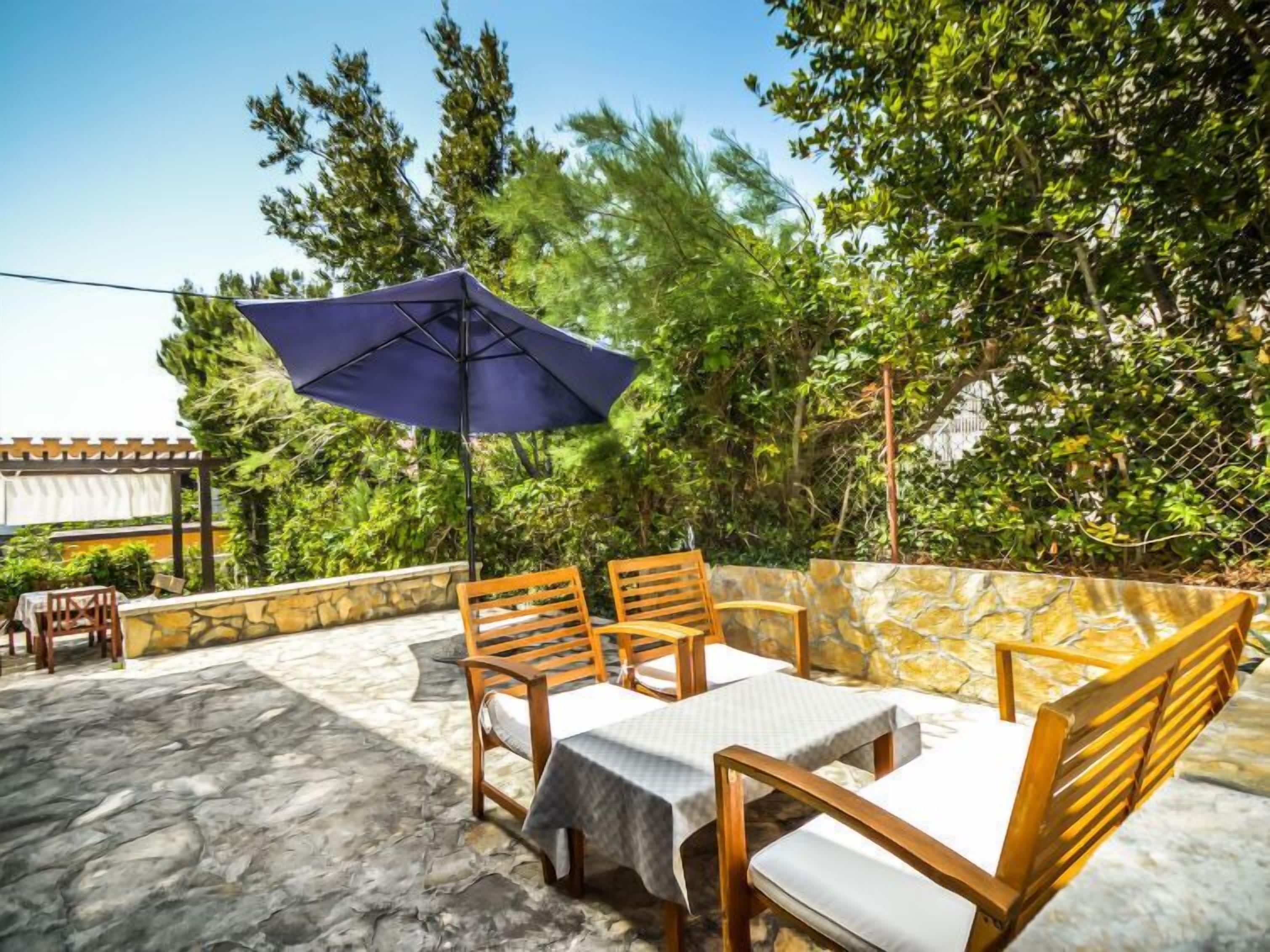 An outdoor patio with stone flooring, wooden furniture, and a large umbrella.