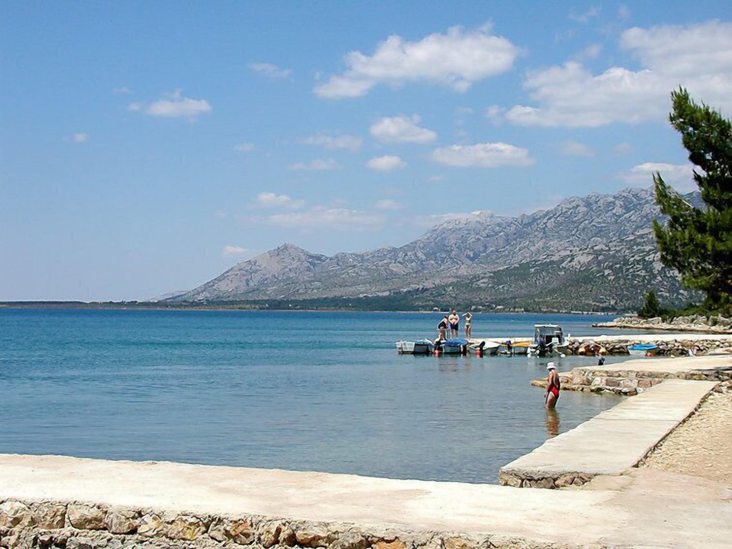 A coastal scene with a clear sky, calm sea, rocky shoreline, and a mountain in the background.