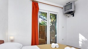 A hotel room with a bed, a TV mounted on the wall, and a window with orange curtains. - Apartment Rubin by Interhome (Hvar/Pokrivenik)