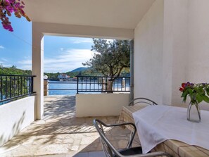 Varanda com mesa e cadeiras, com vista para a água e uma árvore.