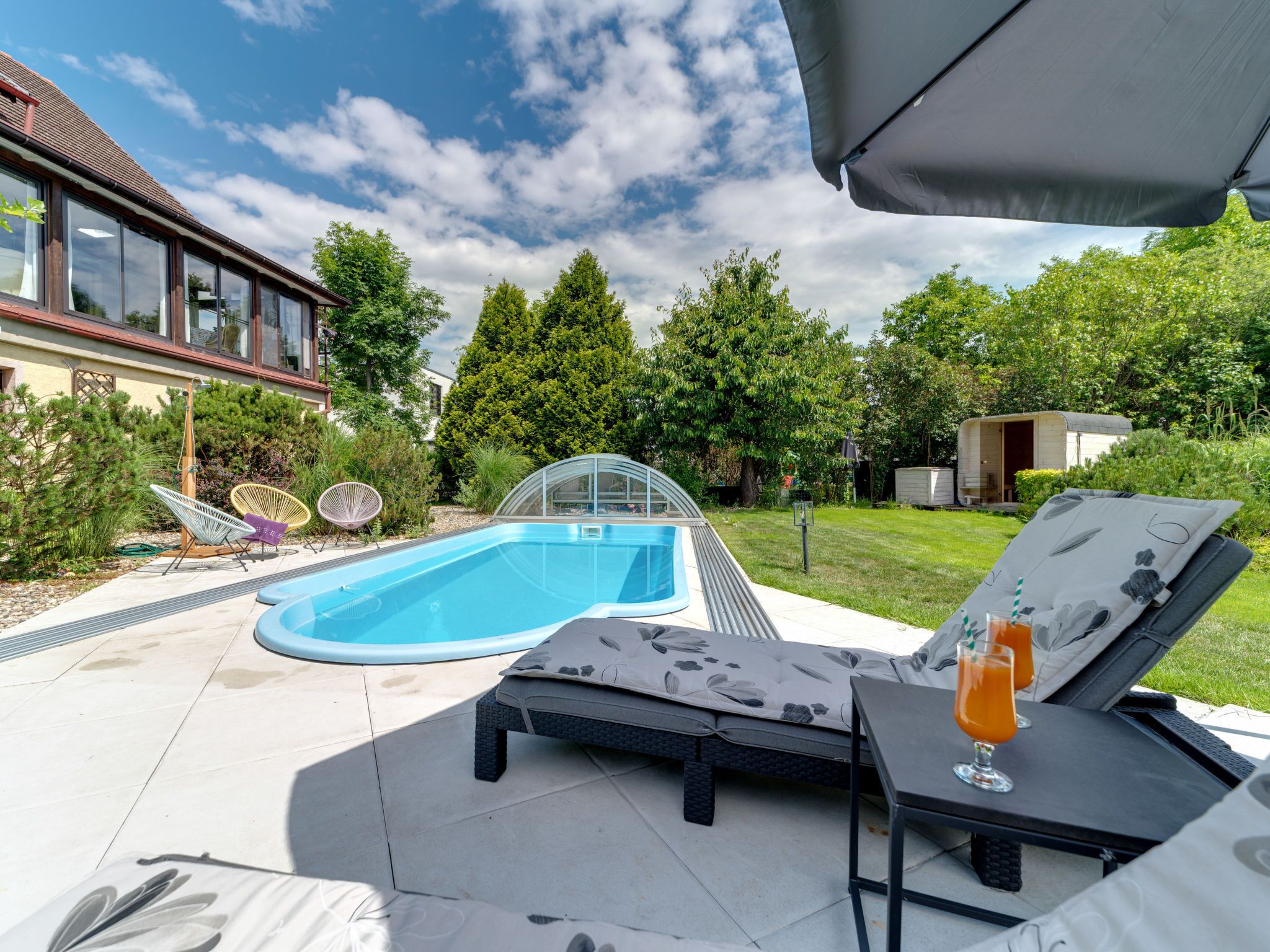 A backyard with a swimming pool, lounge chairs, and a small deck area.