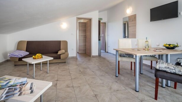 A modern living room with a sofa, a dining table, and a TV mounted on the wall. - Apartment B&B by Interhome (Medulin/Ližnjan)