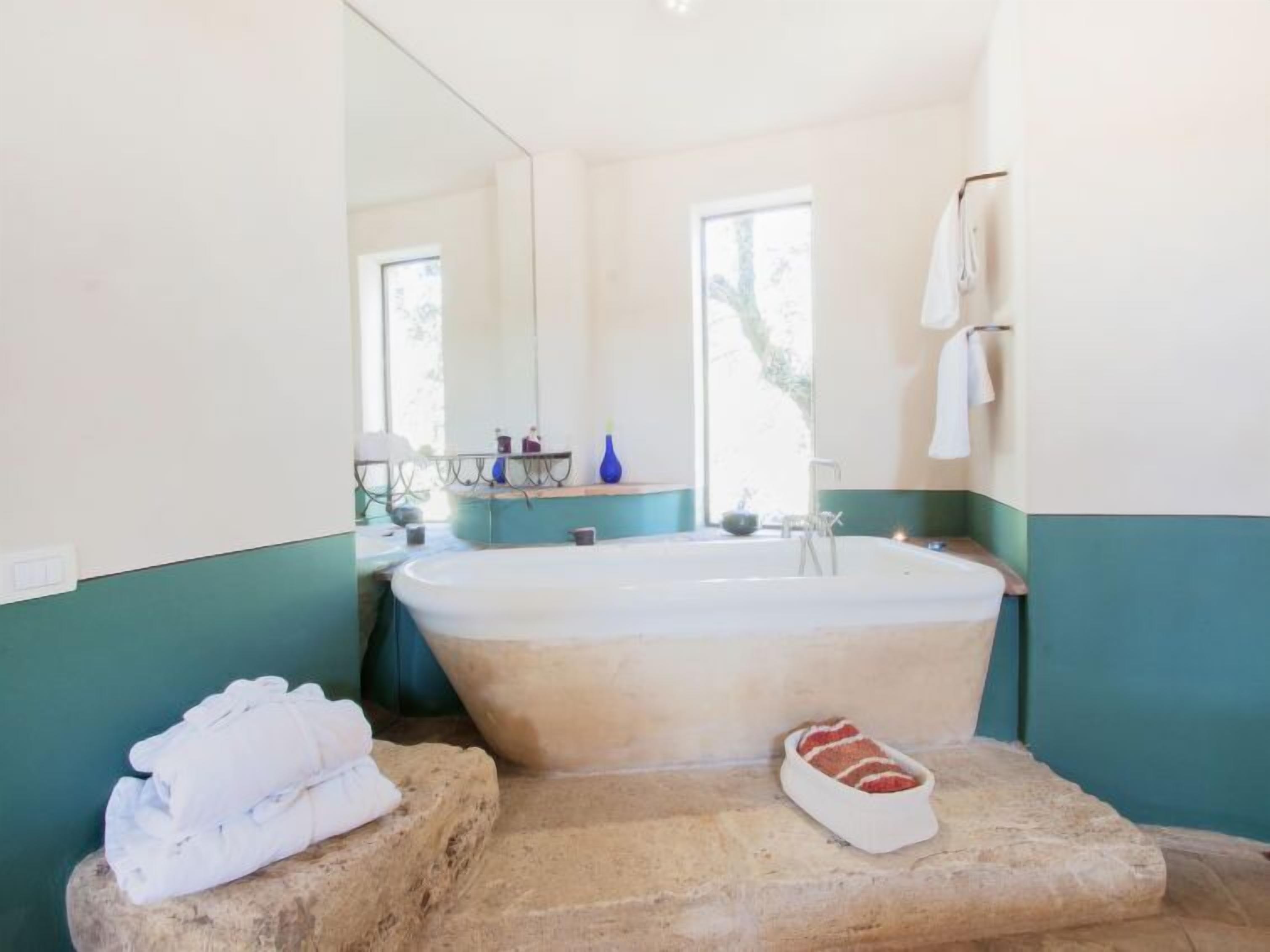 A bathroom with a bathtub, a towel rack, and a stone ledge with a towel and slippers.