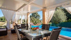 Un espace extérieur aménagé pour les repas, avec une table en verre, des chaises et une vue sur une piscine.