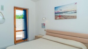 Un dormitorio con cama, una puerta que da a un balcón y un cuadro con una escena de playa en la pared.