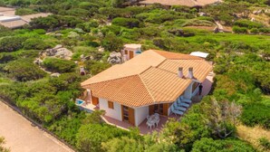 Una casa con techo de tejas, rodeada de abundante vegetación y un camino de entrada pavimentado.