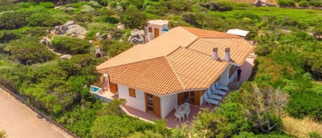 Una casa con tetto in tegole, circondata da rigogliosa vegetazione e un vialetto lastricato.