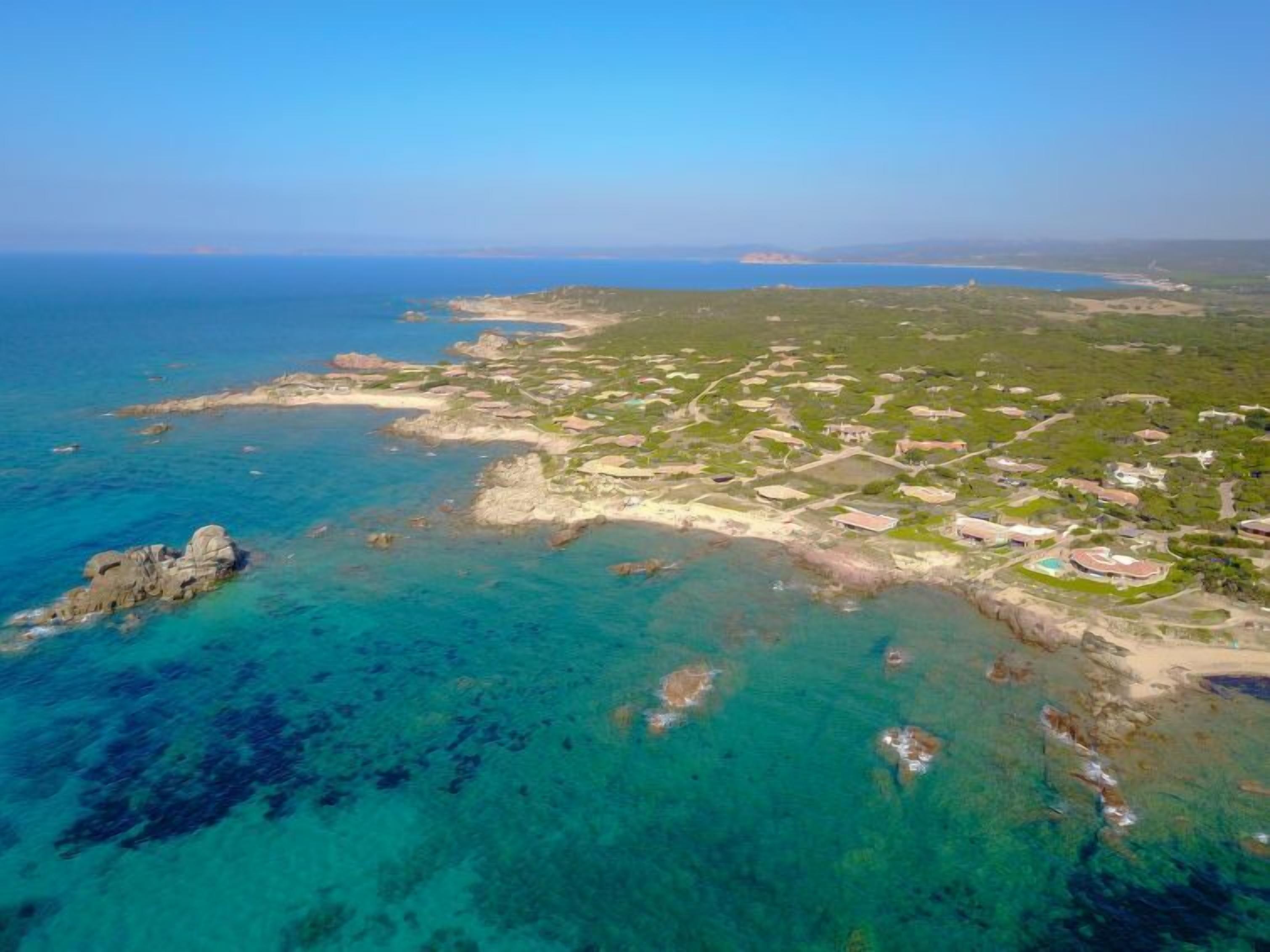 An aerial view of a coastal area with clear blue waters, sandy beaches, and scattered buildings.